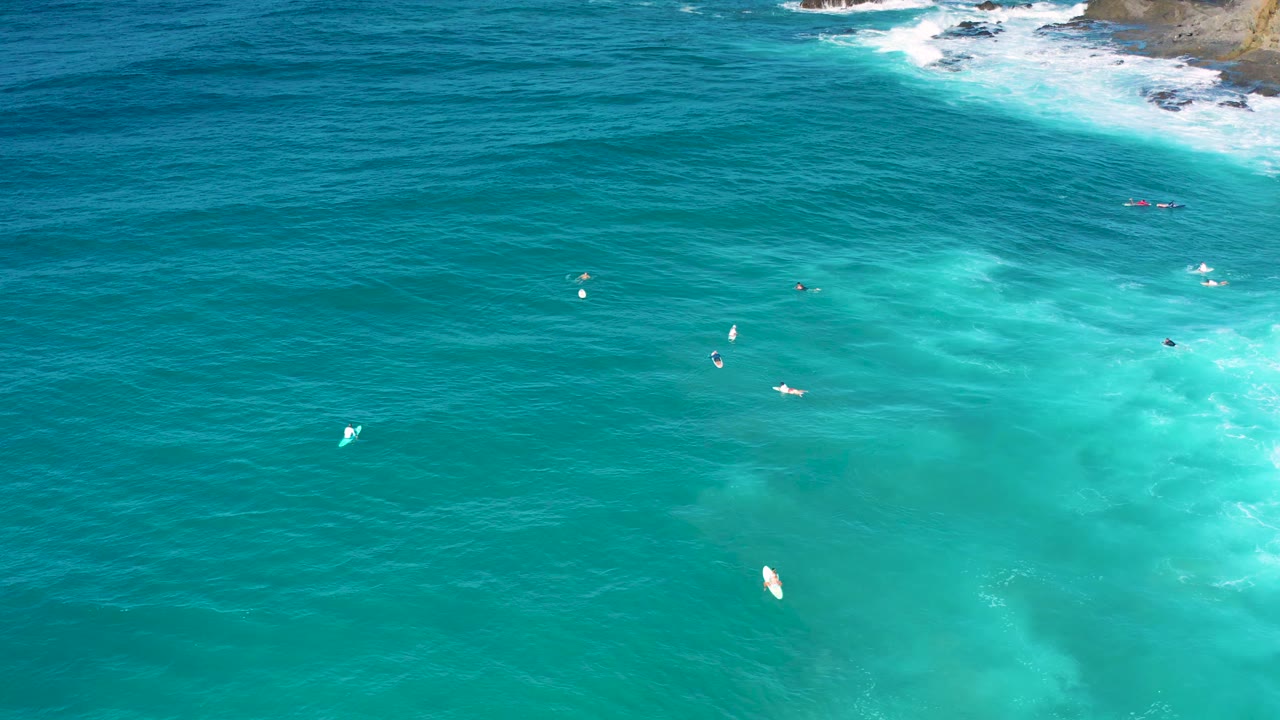 Aerial view at 0:01 over Cerritos water with deeper blue sea across the top, pale turquoise shallows below, white foam near rocks, and no visible people.