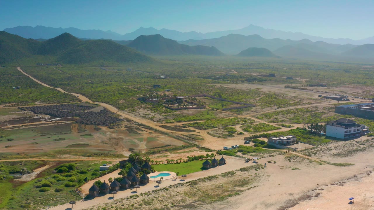 Aerial view over Cerritos, Baja California Sur, with the white building near the lower right edge, the pool nearer center bottom, broad scrubland, and no visible people.