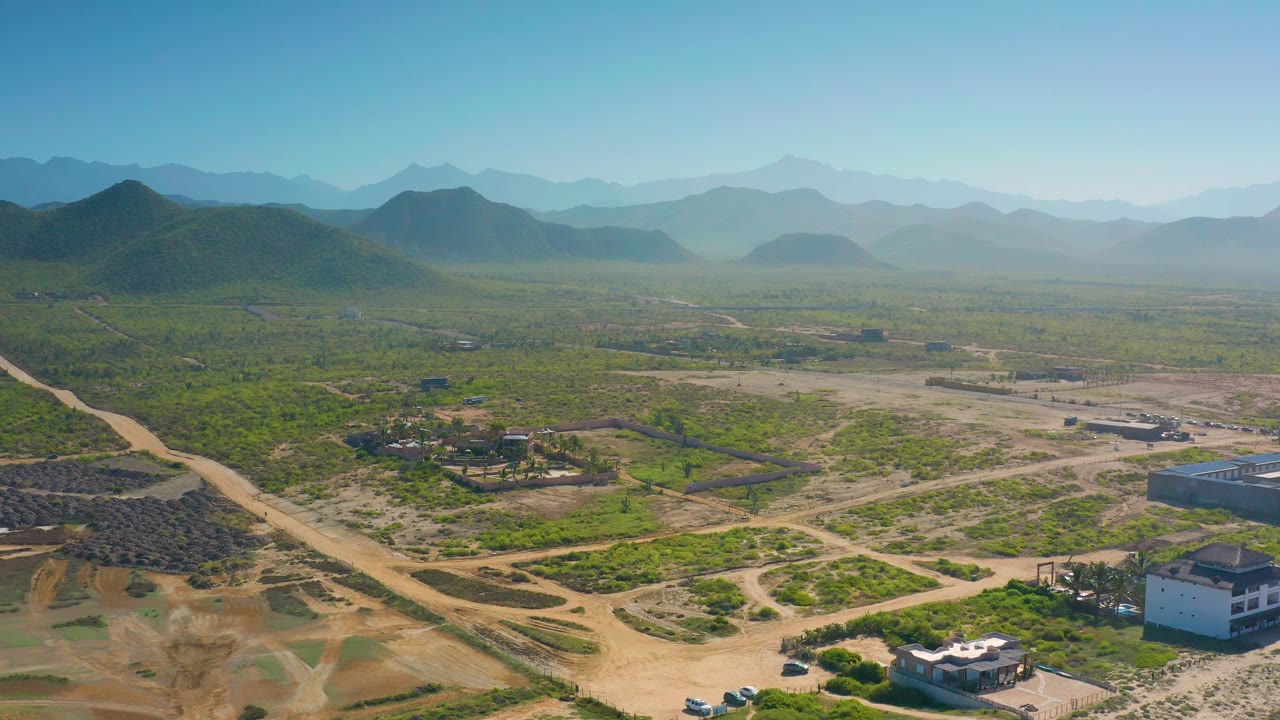 Aerial view of a rural valley with dirt tracks, homes, green land, and hills.