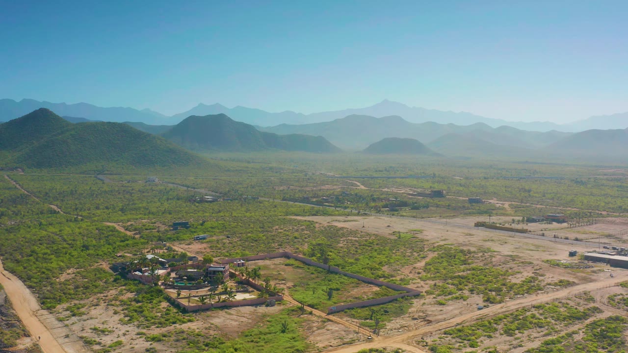 Aerial view of a walled property, sandy roads, green scrub, and mountains