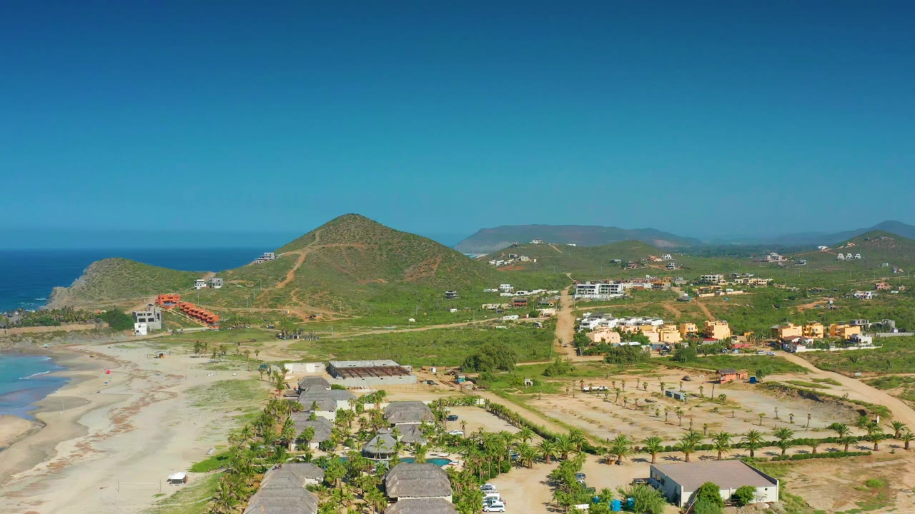 Aerial coastal scene with beach at left and low hills behind homes