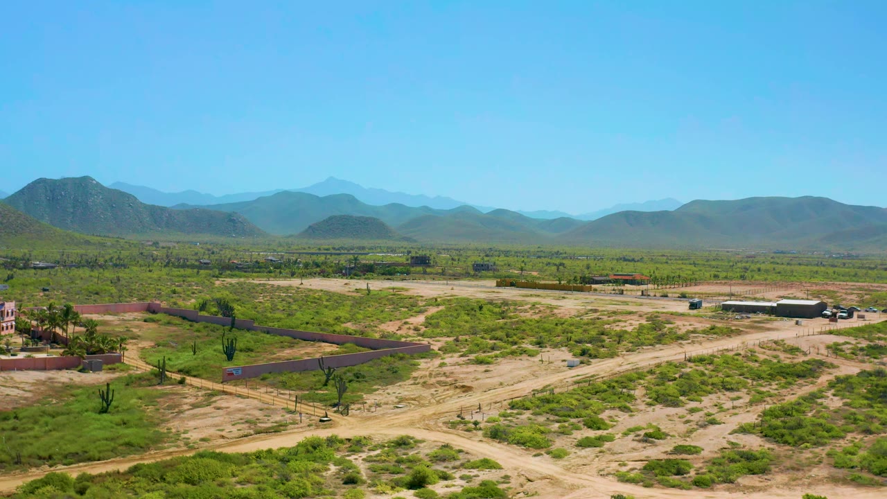 Aerial landscape with a long wall, dirt tracks, scrub vegetation, small structures, and mountains.