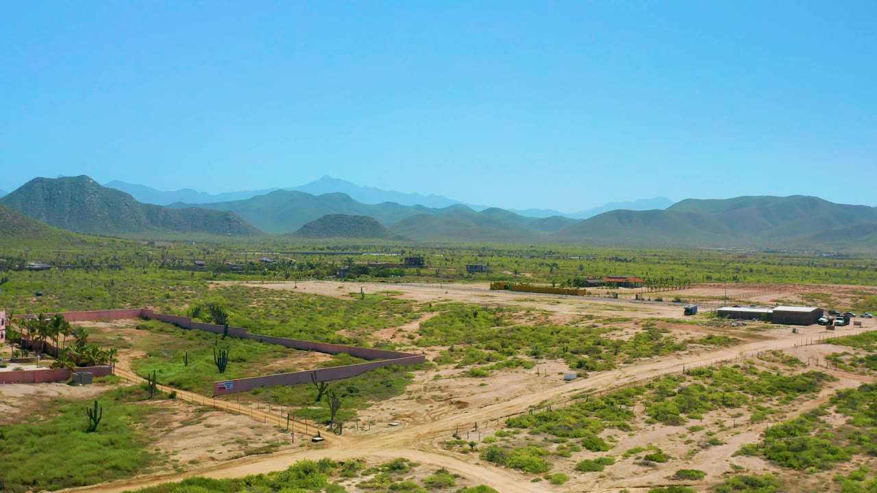 Elevated Cerritos frame with property walls crossing the lower area, pale road grids, green desert vegetation, a few buildings, layered mountains, and no visible people.