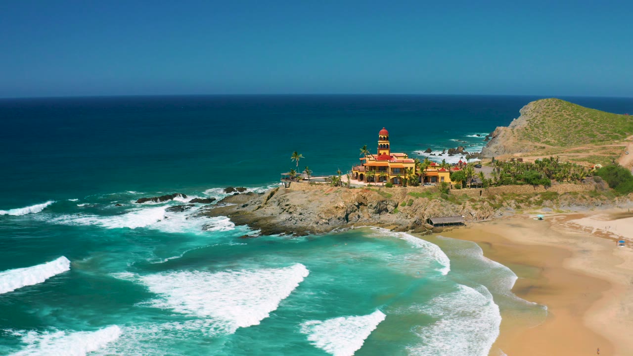 Mid-clip aerial view at Cerritos, Baja California Sur, with the beach taking more of the right side, surf bands crossing the foreground, and no visible people.