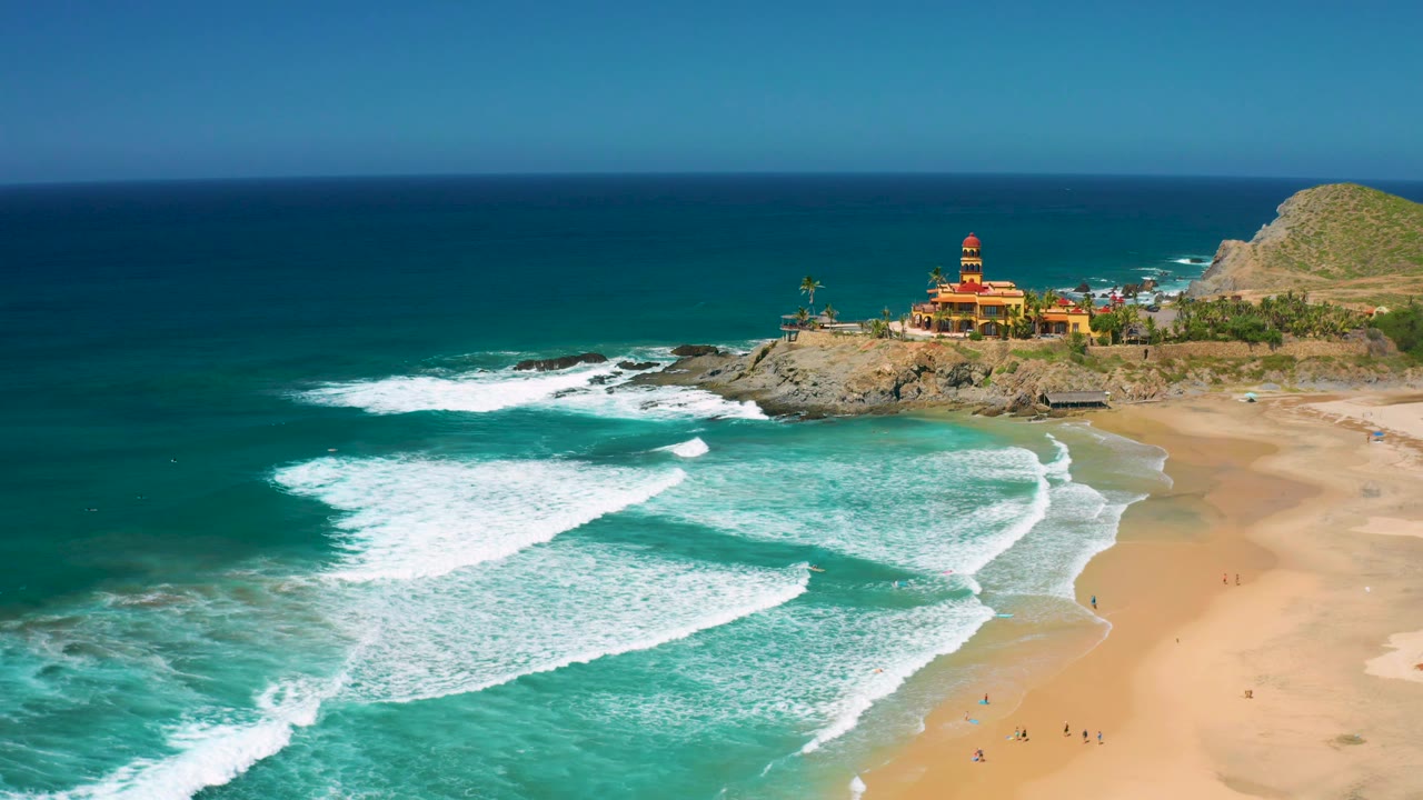 At 0:02, the foam lines sit farther across the shallow turquoise water, with Cerritos beach sweeping along the right side, the rocky point near the top, and no visible people.