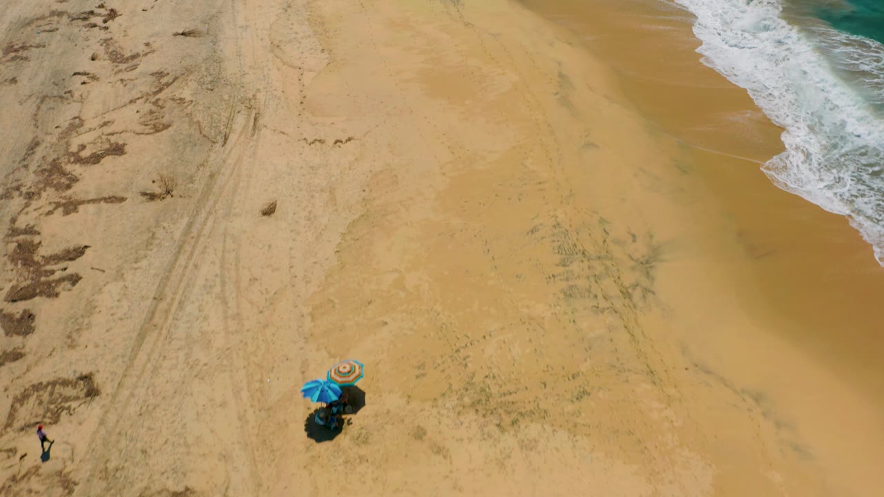 Wide sand field with umbrellas near the lower left and surf at right.
