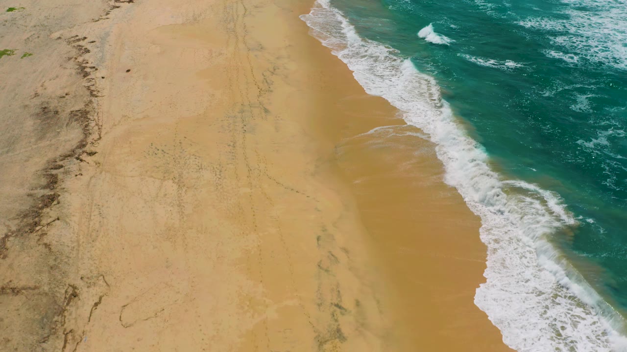 Aerial shoreline with white waves curling onto broad sand.