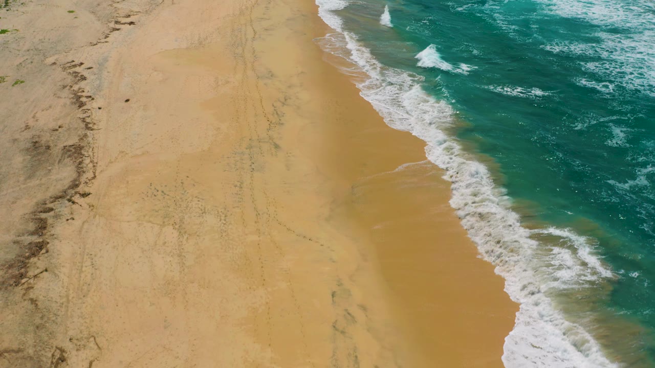 High overhead view at Cerritos beach with the surf line shifted farther right, pale sand exposed across most of the frame, and no visible people.