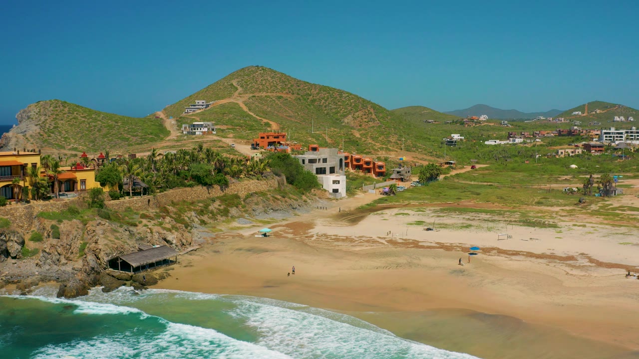 Drone view of beach, ocean foam, homes, and hills