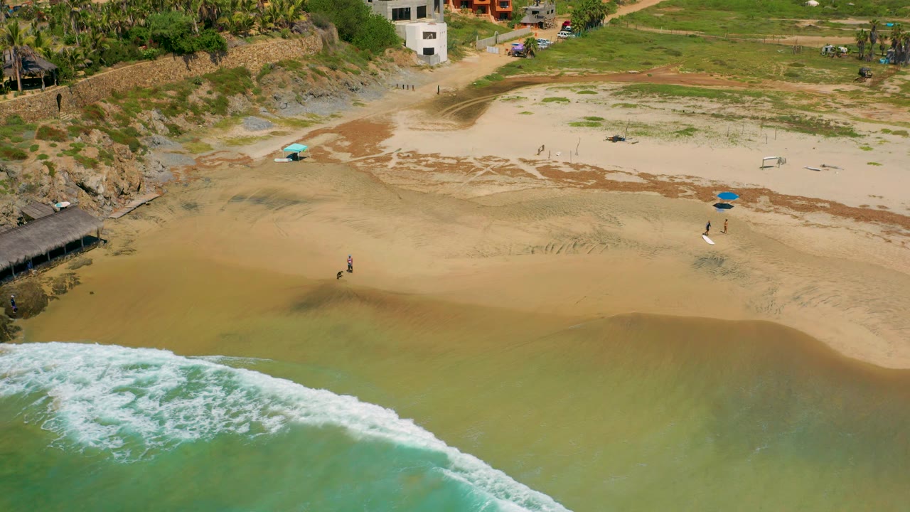 Waves break along the lower edge of a sandy beach with a few small beachgoers visible.