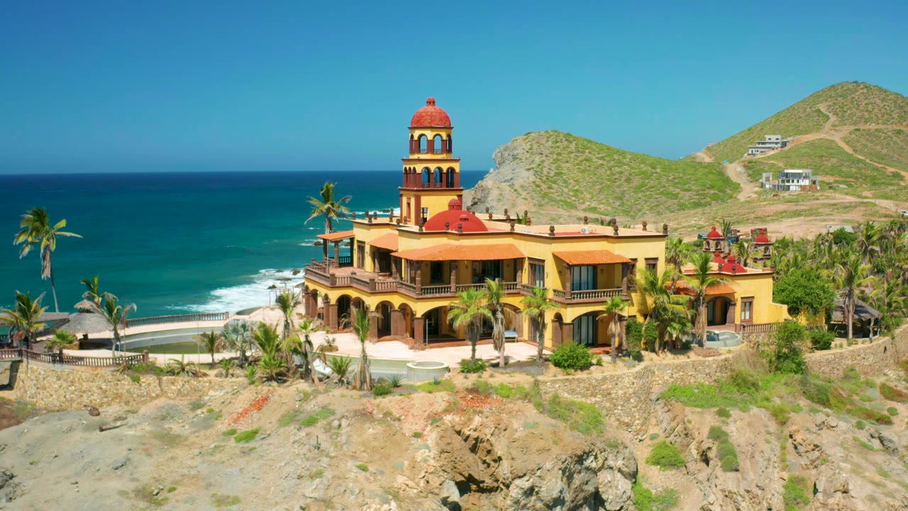 Yellow arched building with red tower above surf and hillside roads.