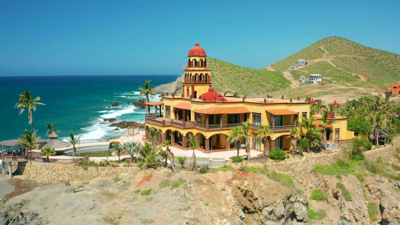 Hillside coastal residence above rocks with waves at left.