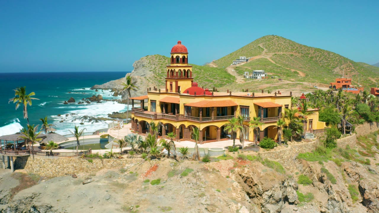 Coastal hillside structure with arched facade above rocky shore
