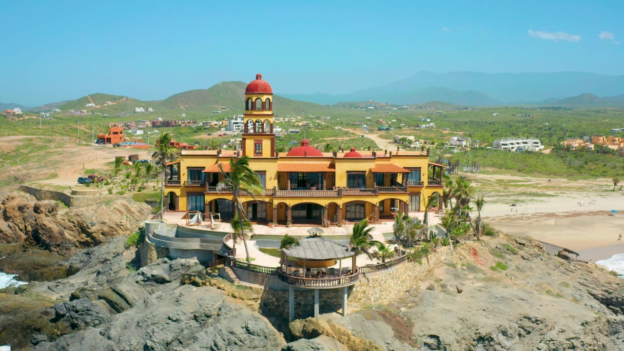 Coastal building beside rocks with inland town in background.