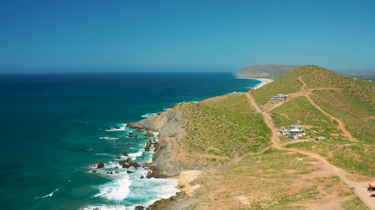 Rocky coast and hillside homes seen from above under clear sky.