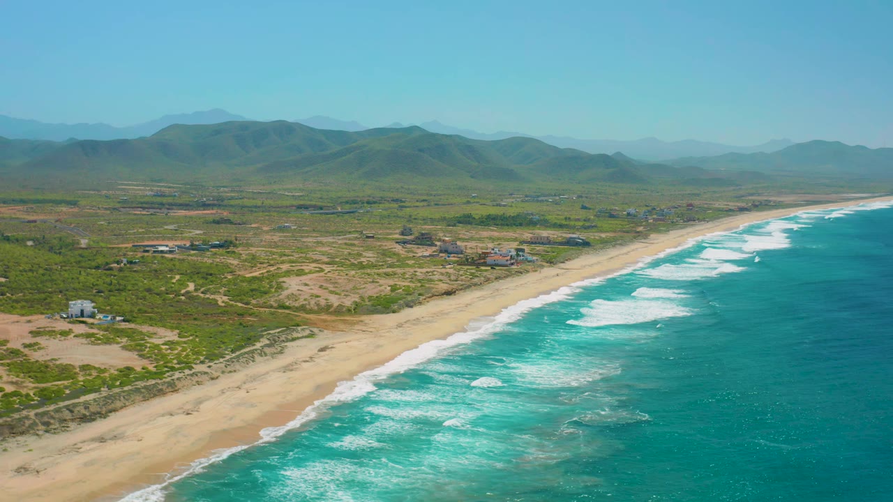 Wide aerial coastline with waves breaking along a long sandy shore.