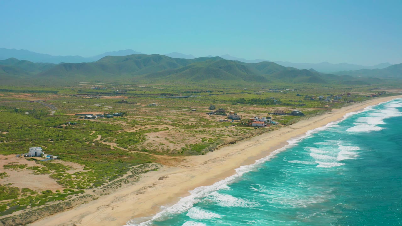 Aerial coastal landscape with surf, sandy shore, houses, and hills