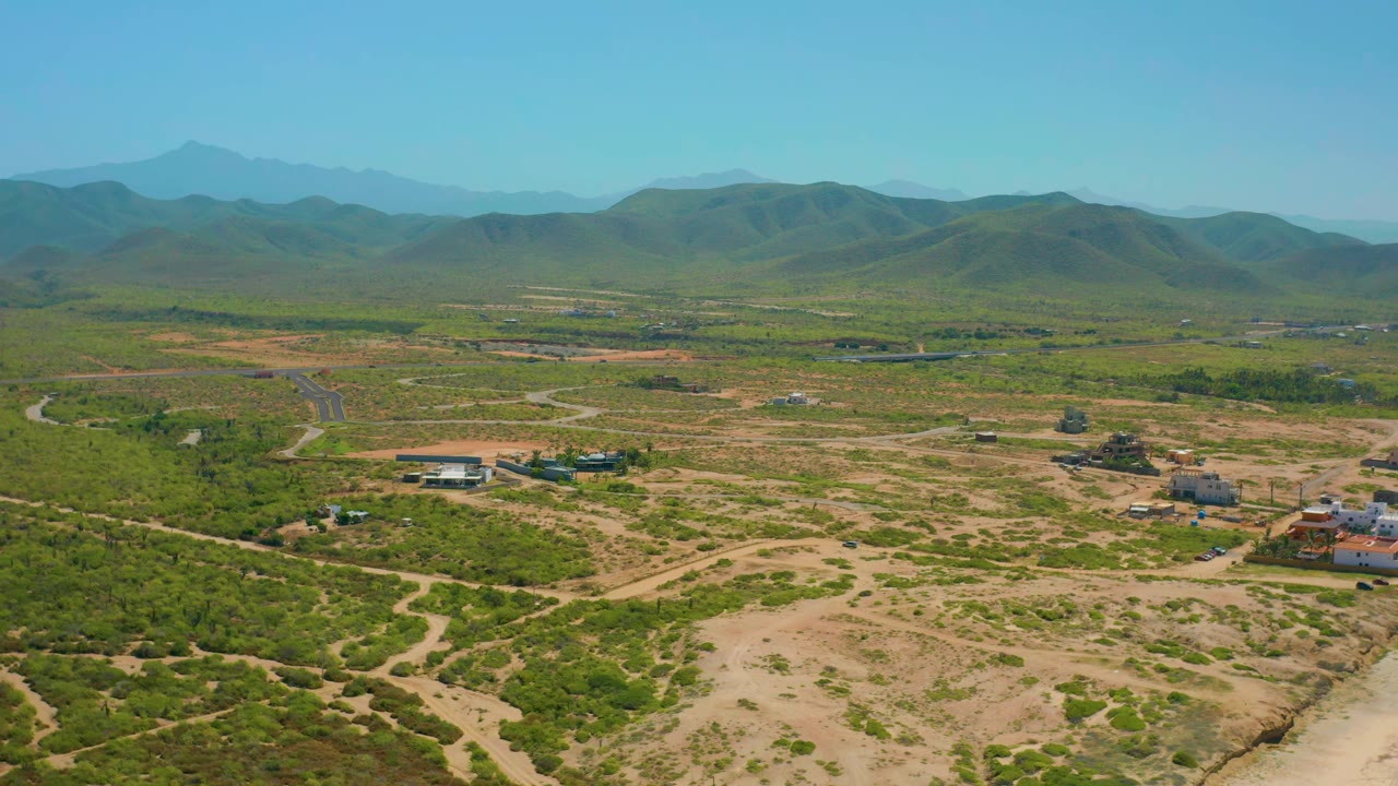 Aerial frame in Cerritos, Baja California Sur, with winding dirt roads in the foreground, scattered structures in the middle distance, layered hills, and no visible people.