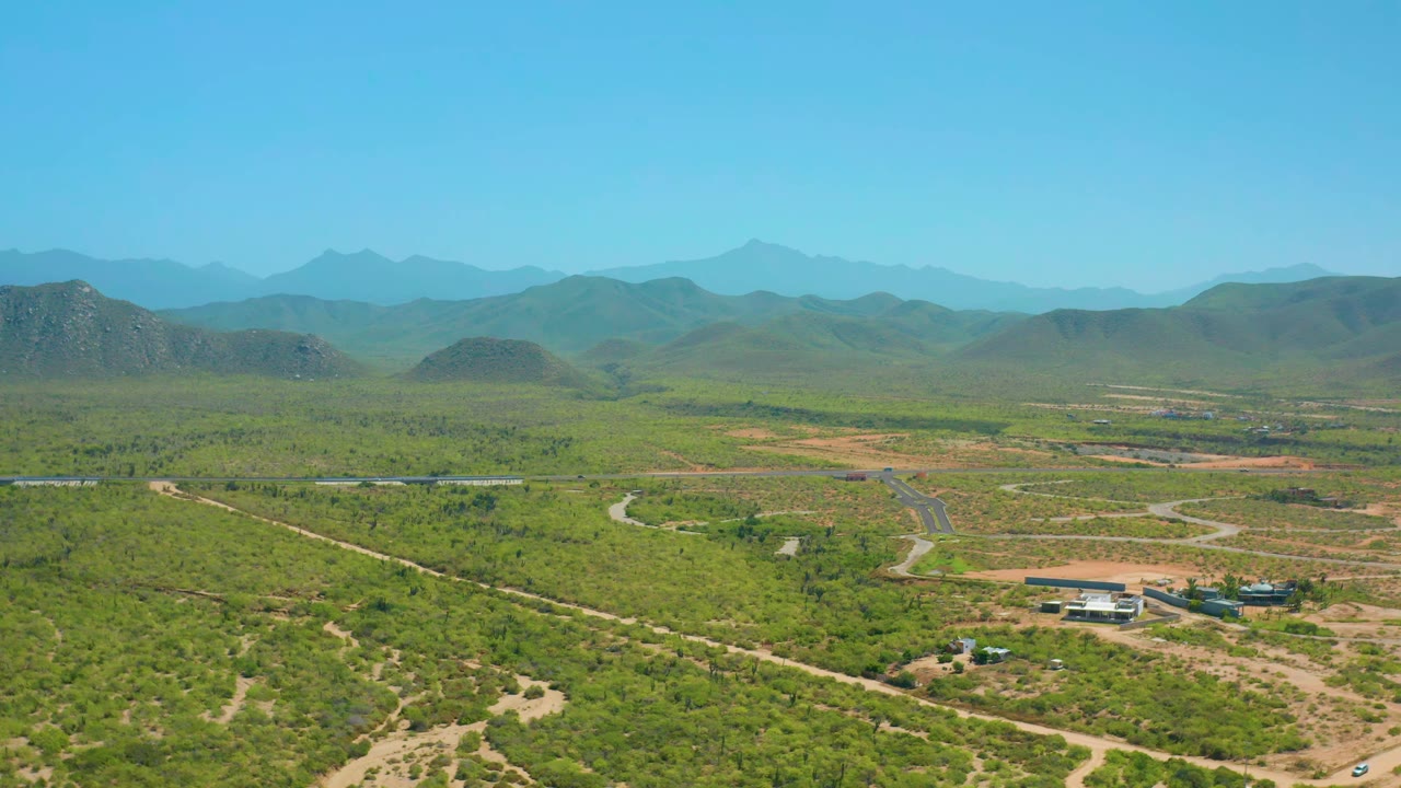 One second into the Cerritos aerial, winding dirt routes and a straight paved road sit among green scrub, with low structures below the hills and no visible people.