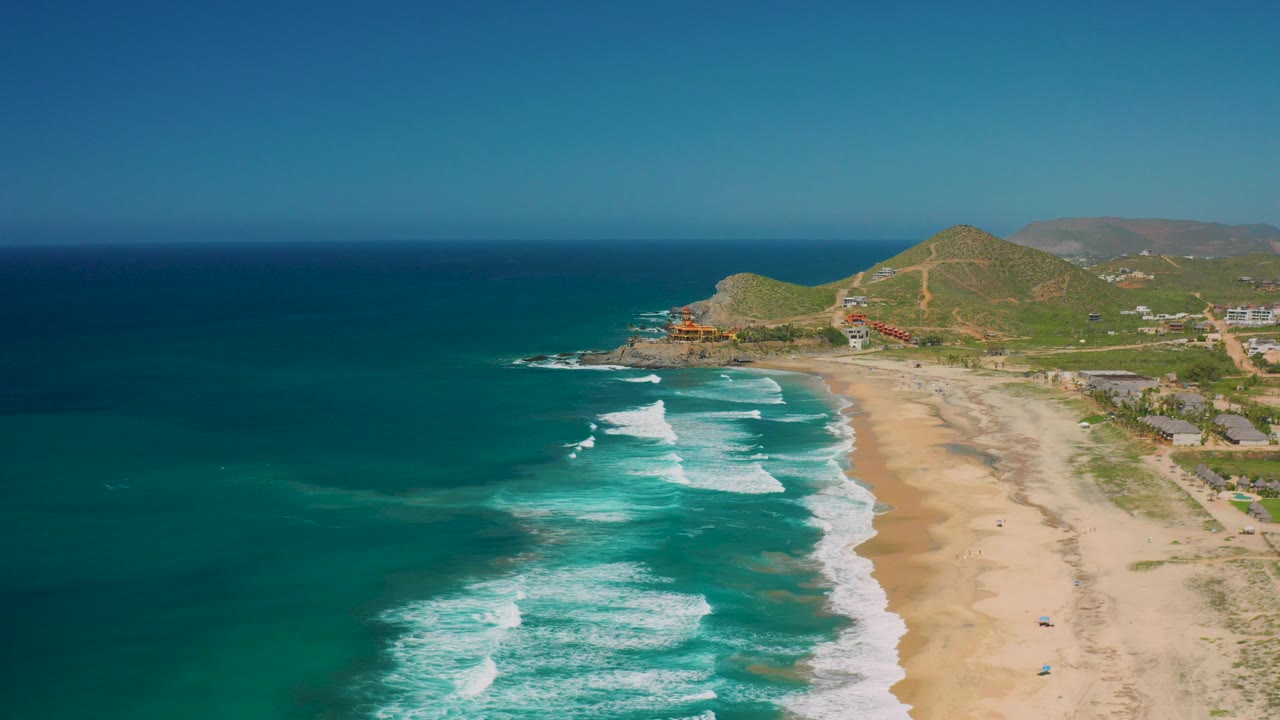 Aerial view of blue ocean waves meeting a sandy beach and green hills.