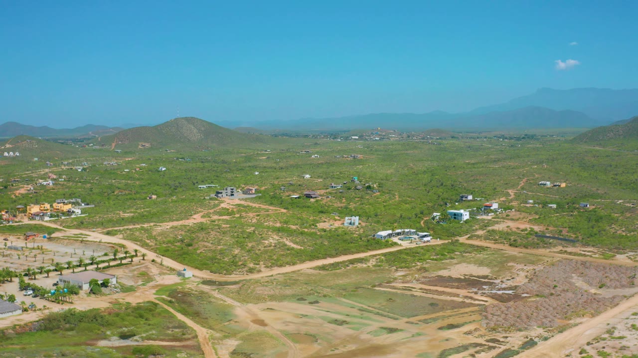 This Cerritos aerial frame keeps the horizon high over pale roads, green brush, scattered houses, low hills, distant mountains, and a clear blue sky with no visible people.
