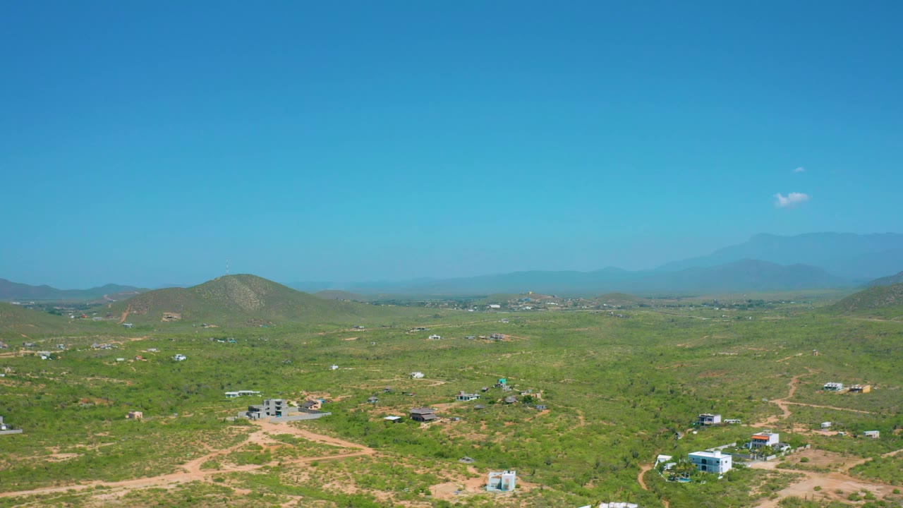 Third frame over Cerritos, Baja California Sur with the horizon set high above green scrub, pale dirt paths, small buildings, rounded hills, and no visible people.