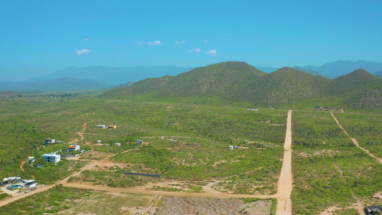 Drone-height view of scrubland roads and rounded hills under blue sky.
