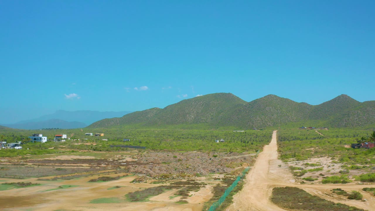 Wide rural landscape with dirt road, green hills, and clear sky.