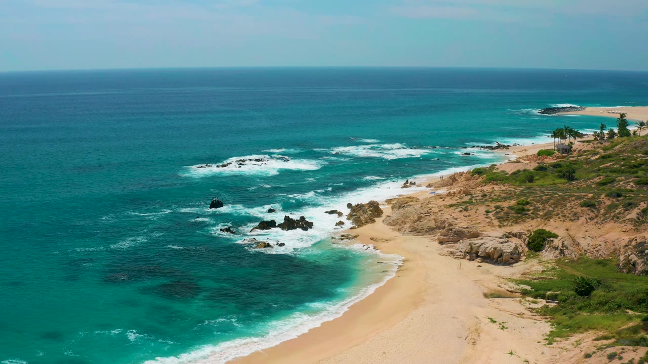 Bird's-eye coastal view with waves breaking around offshore rocks and sand.