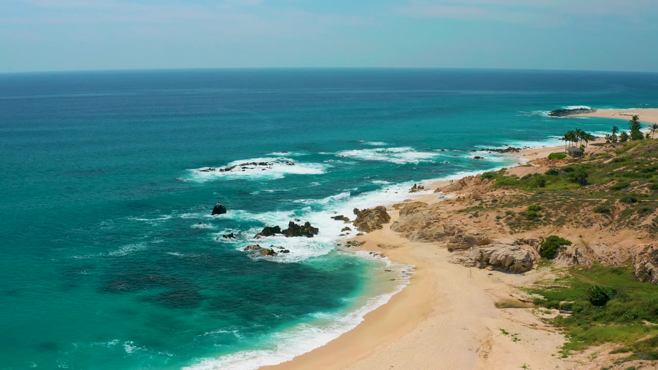 A high view over Secrets Marquis Los Cabos, Mexico shows darker reef patches under turquoise water, a pale sand beach, rocky headland, and no visible people.