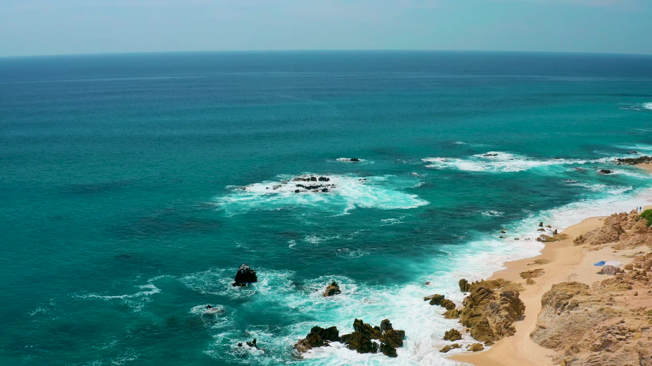 Aerial coastal view at Secrets Marquis Los Cabos, Mexico, with scattered rock outcrops, breaking waves, beach and rocky dunes to the right, and no visible people.