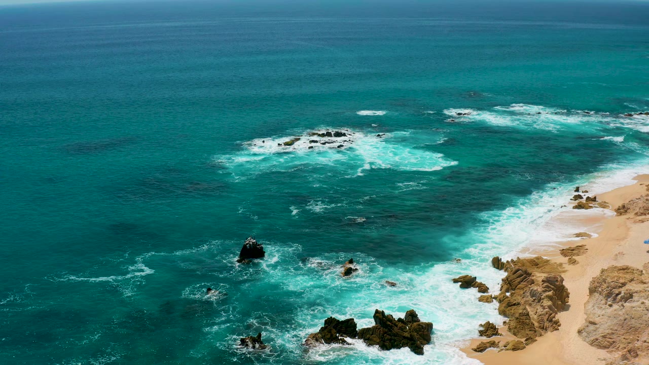 Aerial surf lines around dark rocks with beach on the right.