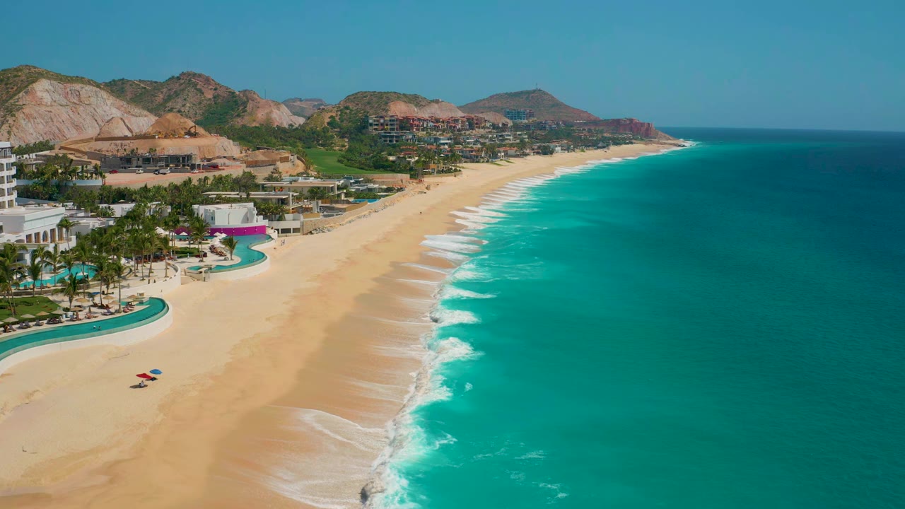 Turquoise shoreline with resort grounds and low mountains in the background.
