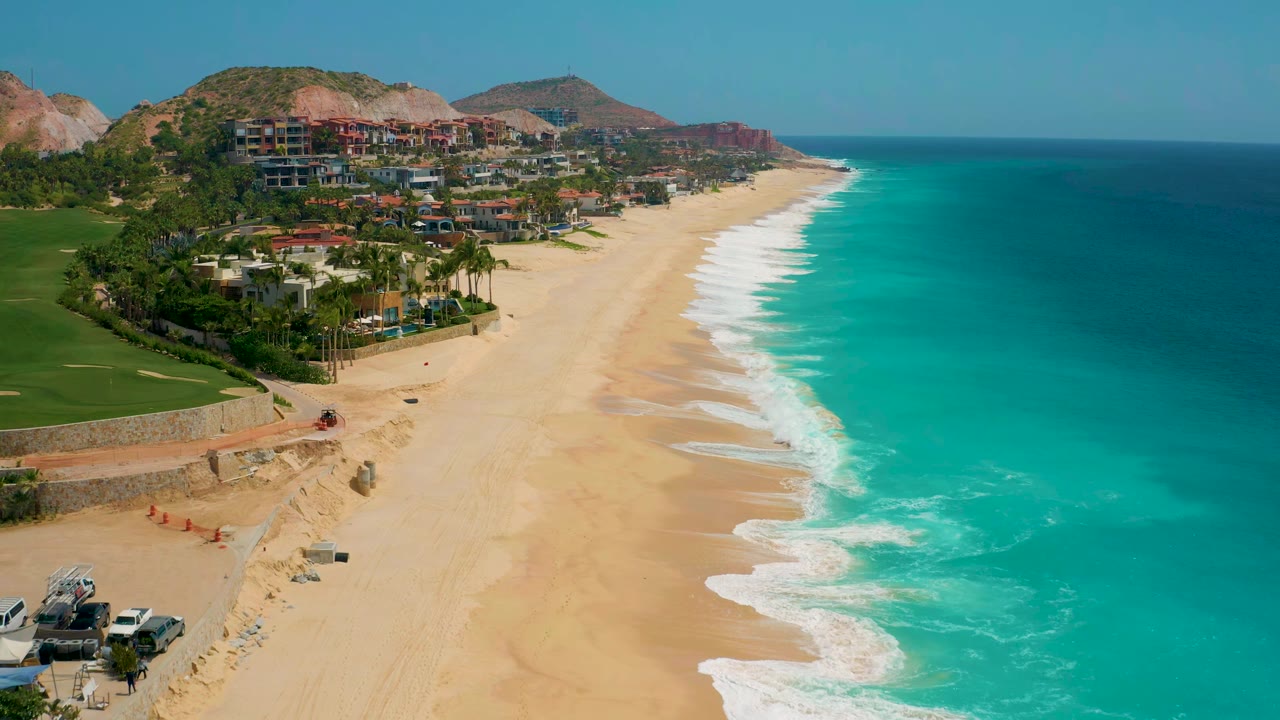 Wide coastal aerial with waves washing along an empty sandy beach.