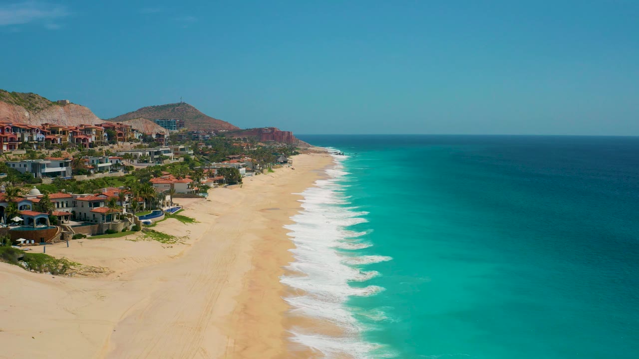 At 0:03, the aerial angle shows the Secrets Marquis Los Cabos coast stretching away, with repeating white wave edges along the sand and no visible people on the beach.