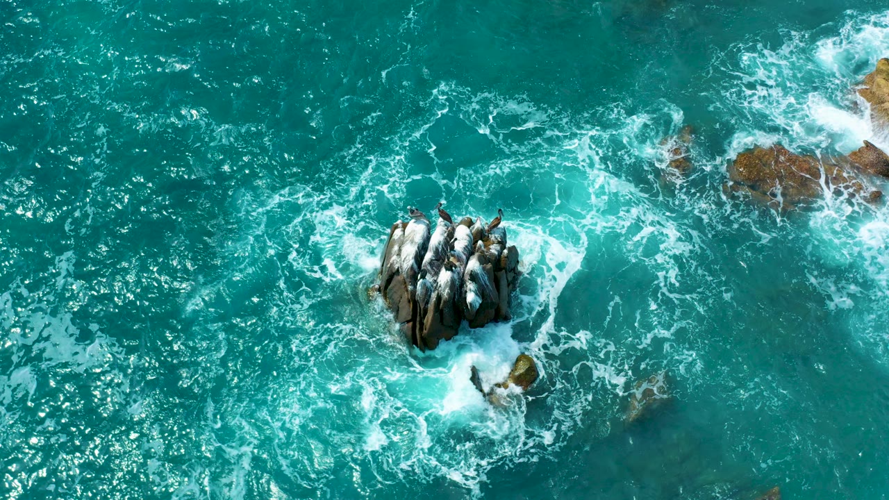 Overhead blue ocean water breaking around a central rock cluster