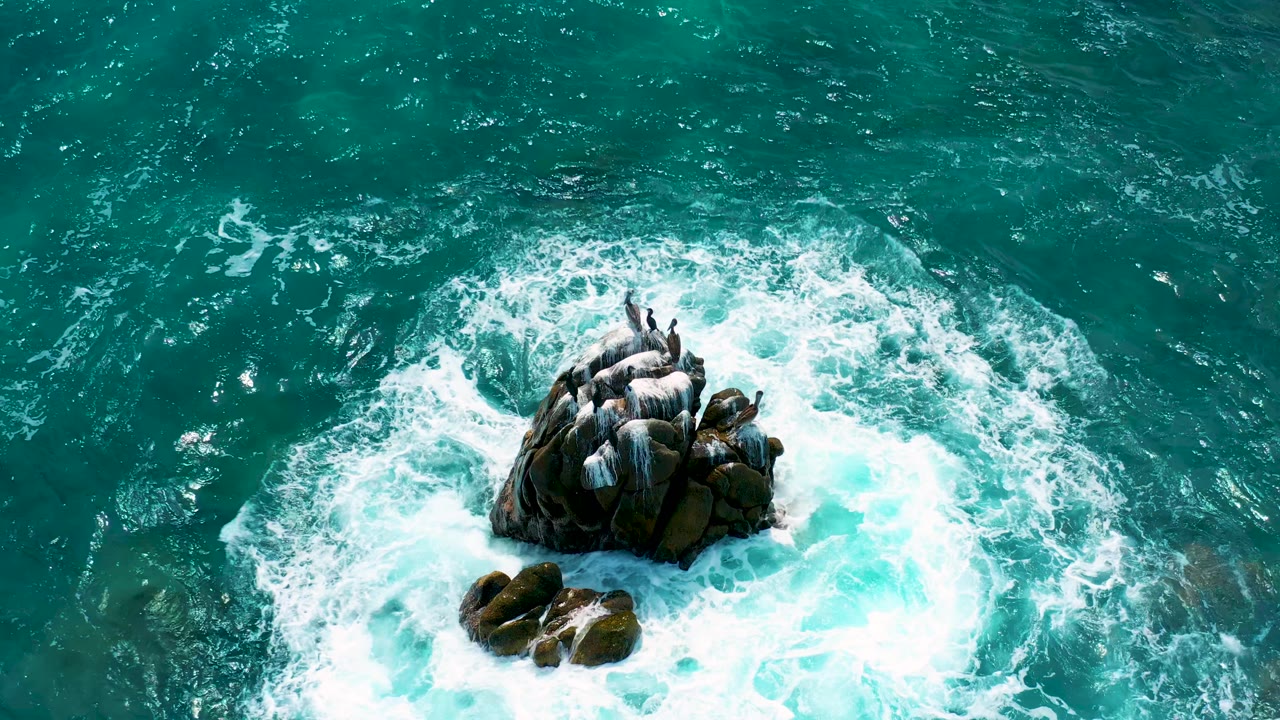 White surf curls around a central rock outcrop in teal water.