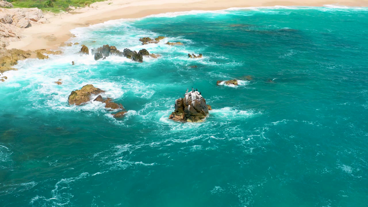 Aerial view at Secrets Marquis Los Cabos, Mexico, with turquoise water, white surf, tan beach, scattered rocks, and no visible people.