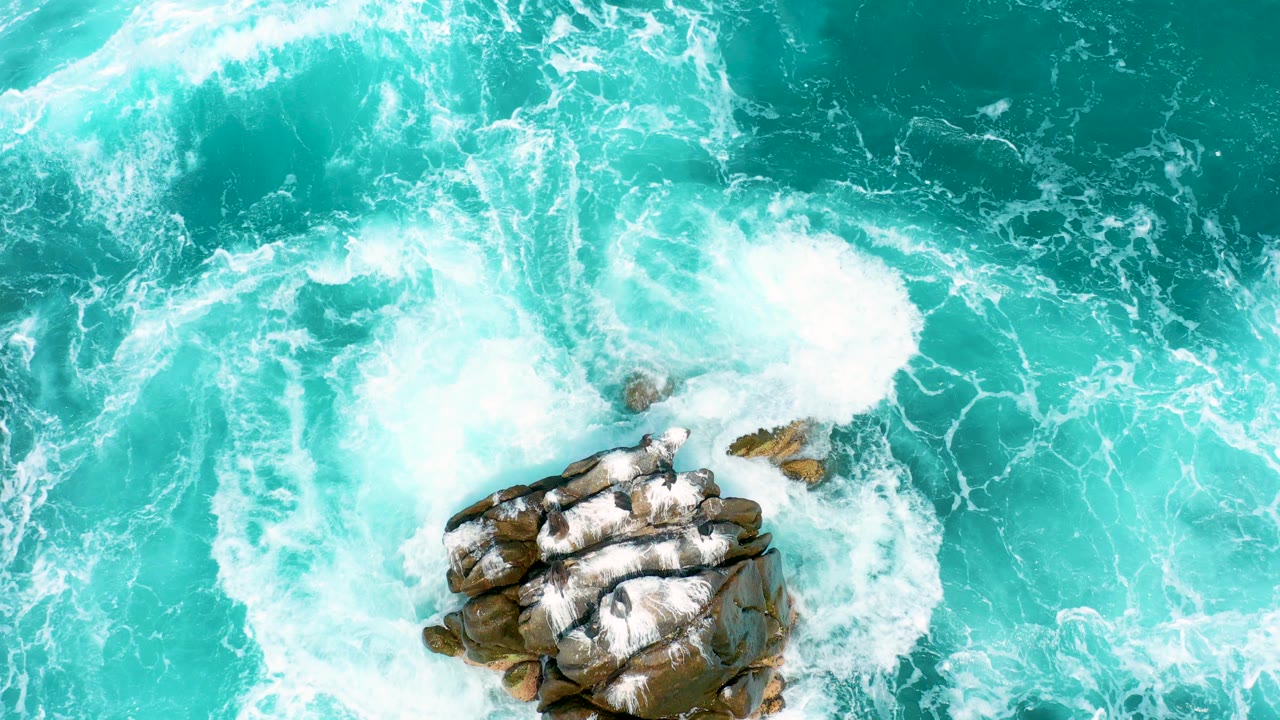 Overhead view of turquoise water and white foam breaking around dark rocks at Secrets Marquis Los Cabos, Mexico, with no visible people.