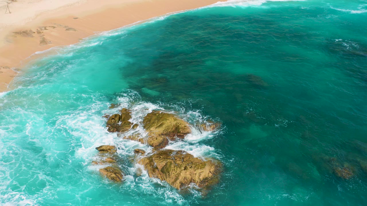 Aerial view at Secrets Marquis Los Cabos, Mexico showing turquoise water, tan beach at the top, rocky outcrops below center, white surf, and no visible people.