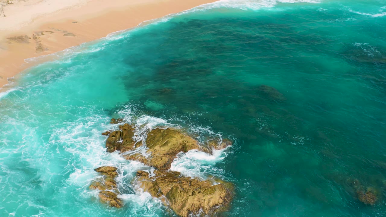 Aerial view at Secrets Marquis Los Cabos, Mexico showing the beach across the upper frame, broad turquoise water, rocky surf lower in frame, and no visible people.