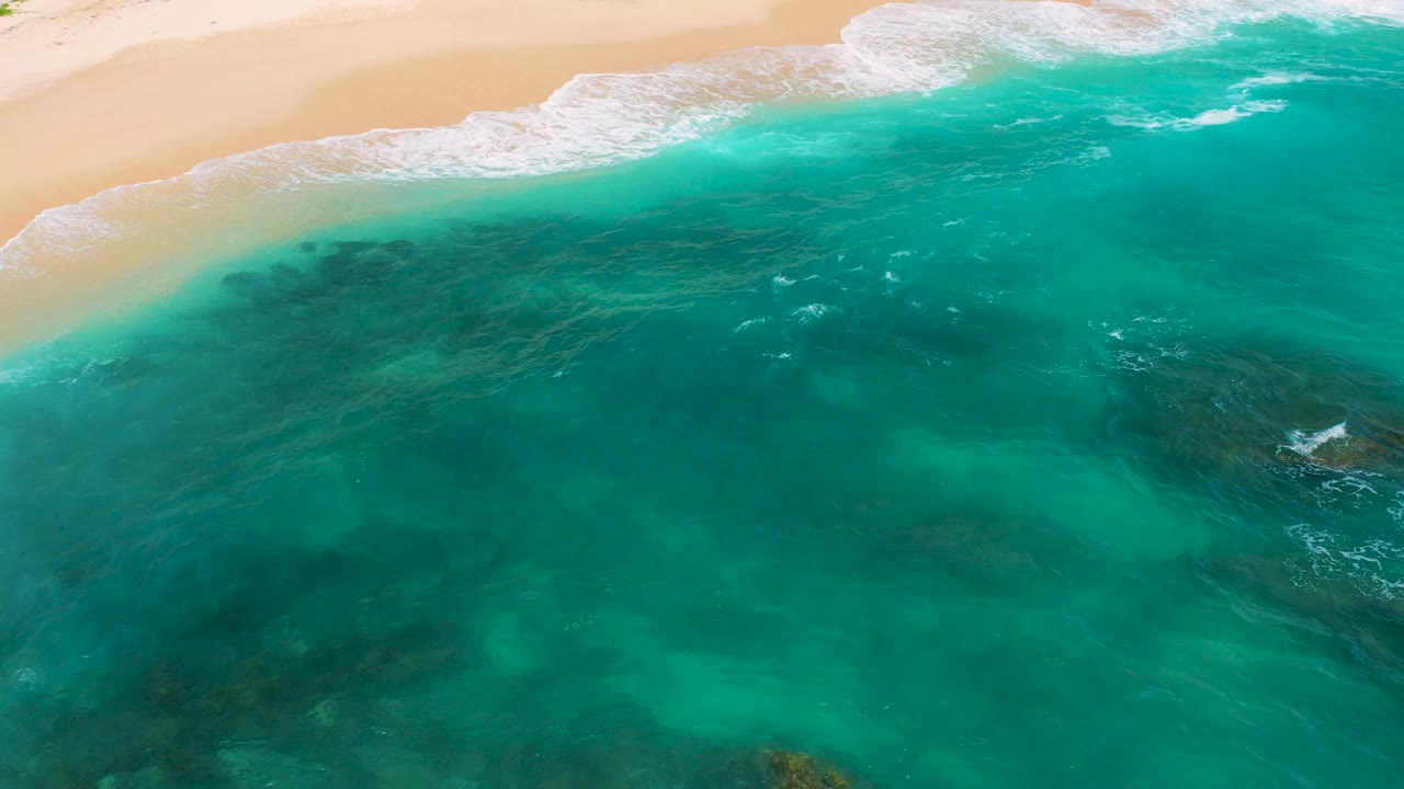 Overhead view at Secrets Marquis Los Cabos, Mexico, showing tan beach along the top, white surf, turquoise water, darker submerged patches, and no visible people.