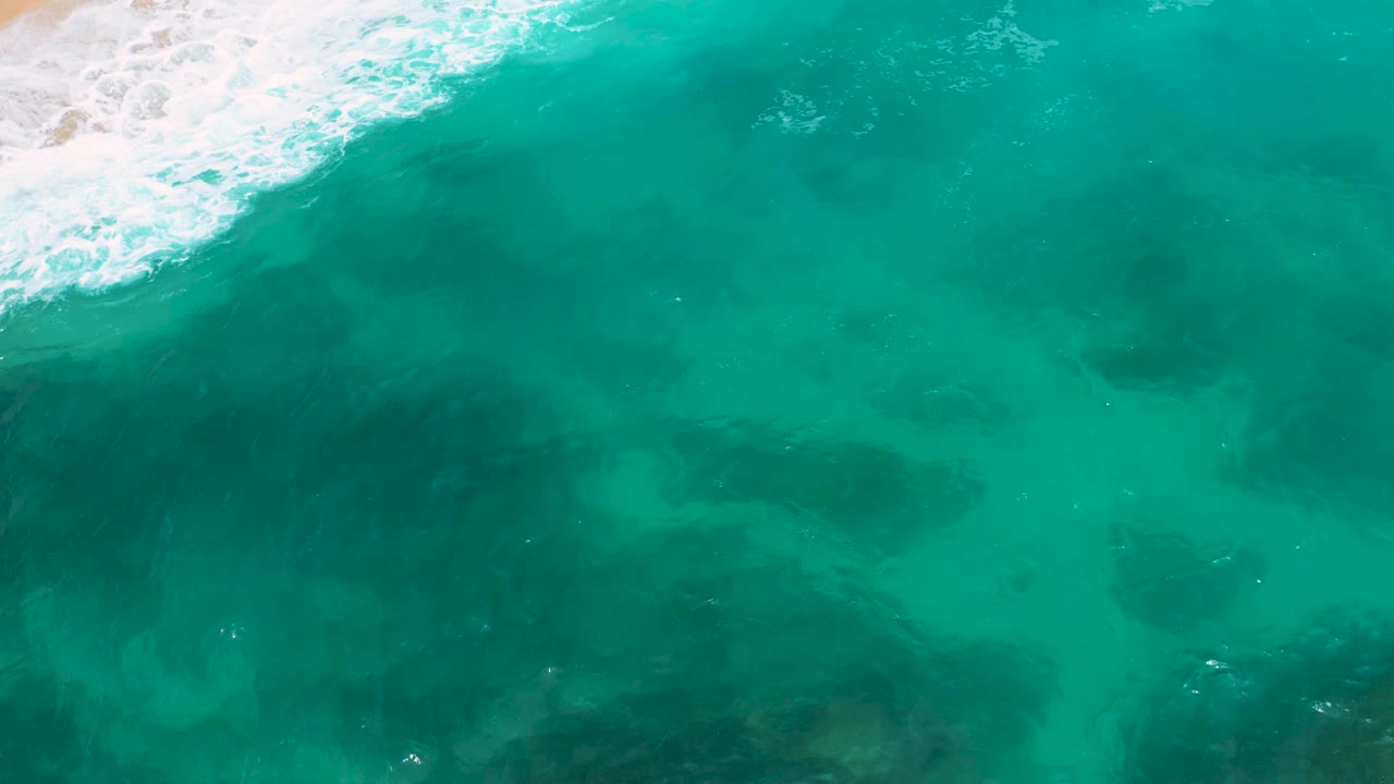Clear green-blue water with surf foam along the upper shoreline.