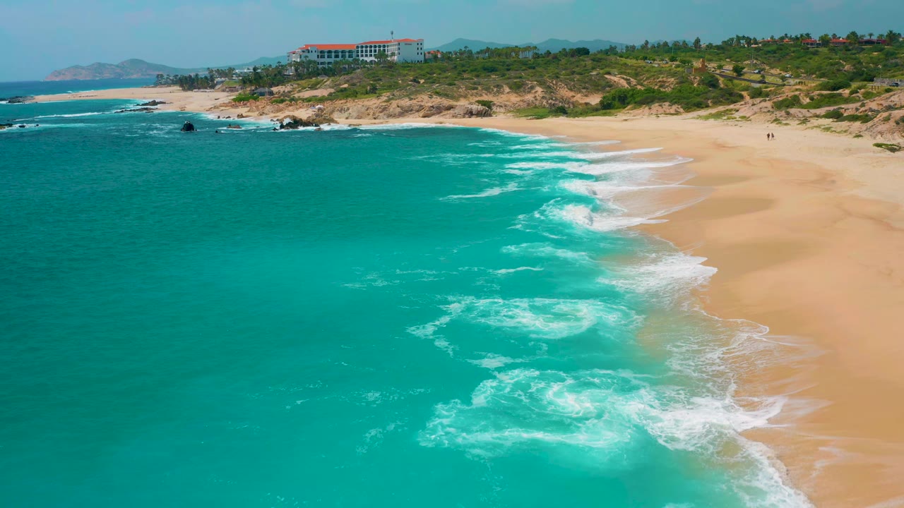 Turquoise water and white wave lines along a broad beach.