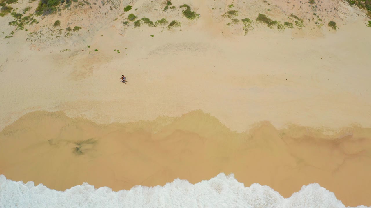 Top-down sandy beach with a lone walker and low waves near the bottom edge.