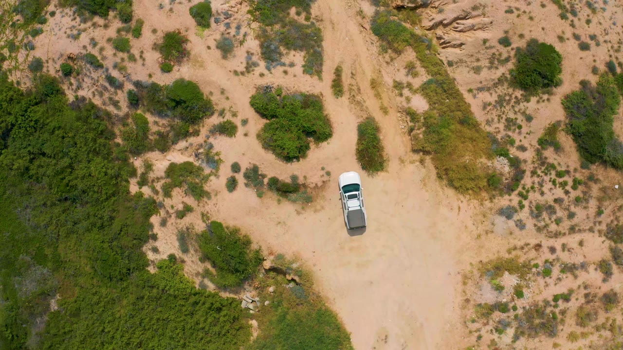 Overhead frame from Secrets Marquis Los Cabos, Mexico showing a white truck on a sandy track beside dense green bushes and scrub, with no visible people.
