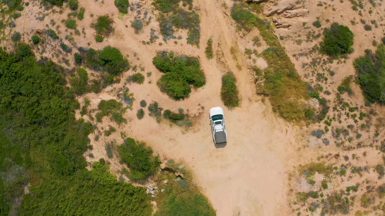 The aerial frame shows a white truck near the right side of a sandy clearing in Secrets Marquis Los Cabos, Mexico, with thick green vegetation on the lower left and no visible people.