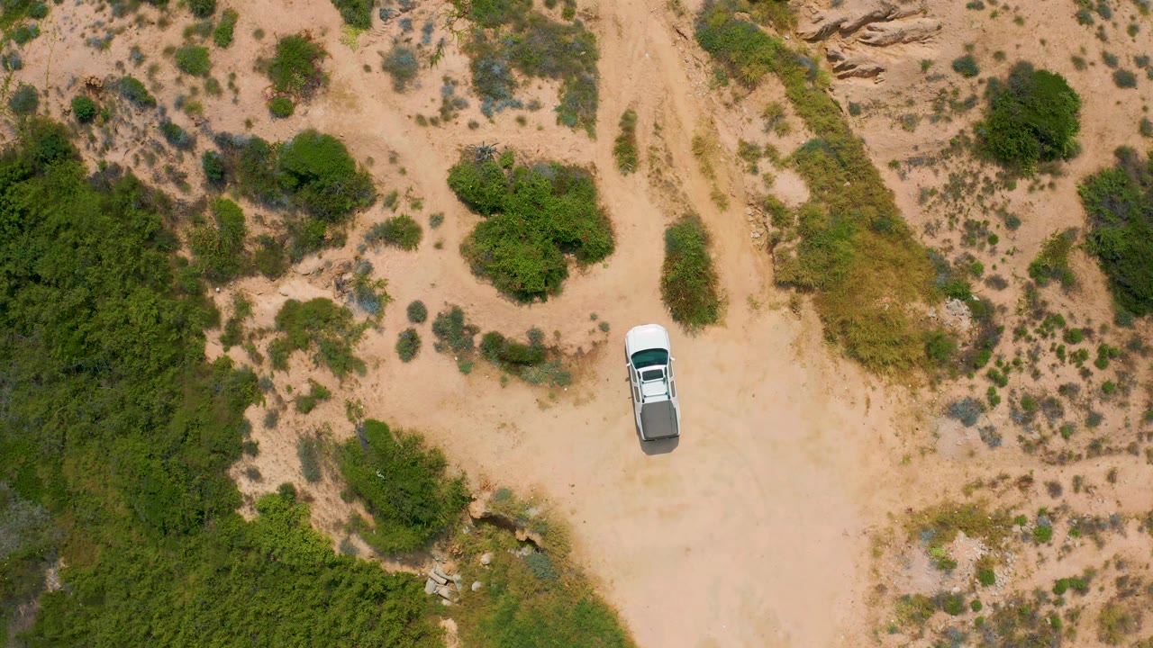 White truck on sand beside dense green vegetation and scrub.
