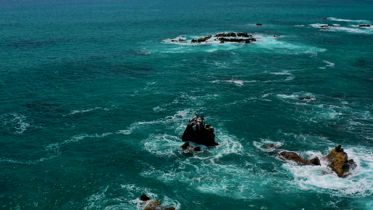 Aerial view near Secrets Marquis Los Cabos, Mexico, showing blue-green ocean water breaking around dark offshore rocks with no visible people.