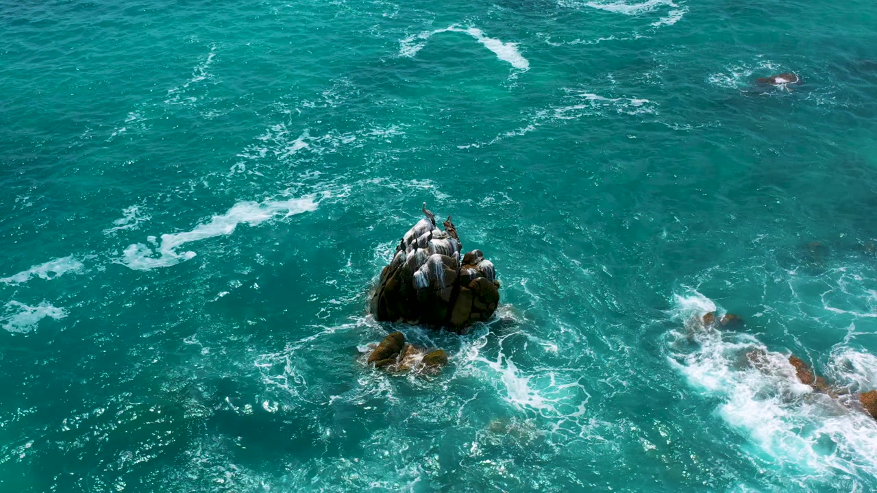 Rock outcrop in blue-green water with foam curling over submerged rocks.
